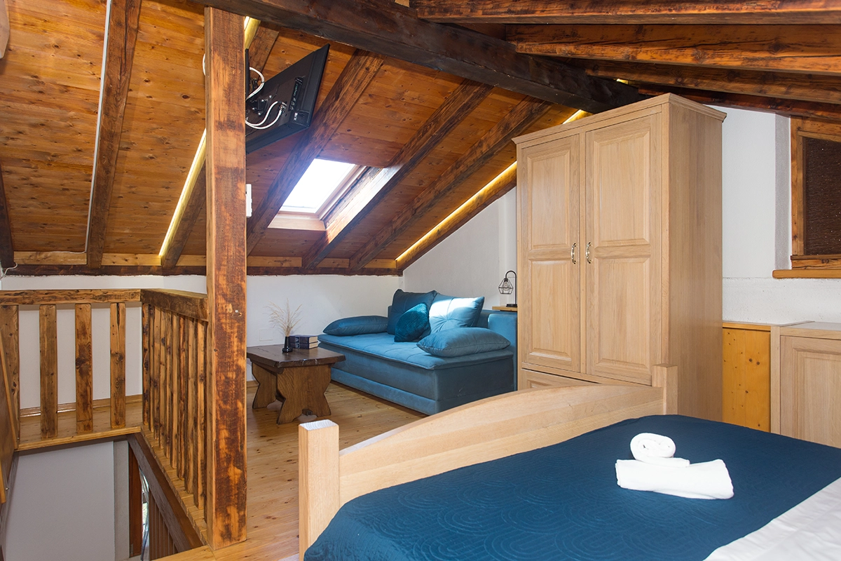 Room with a double bed and sofa, in the attic, featuring a wooden wardrobe and parquet flooring.